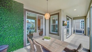 Uma área de refeições com uma mesa de madeira e cadeiras de vime, um lustre pendurado e uma parede verde.