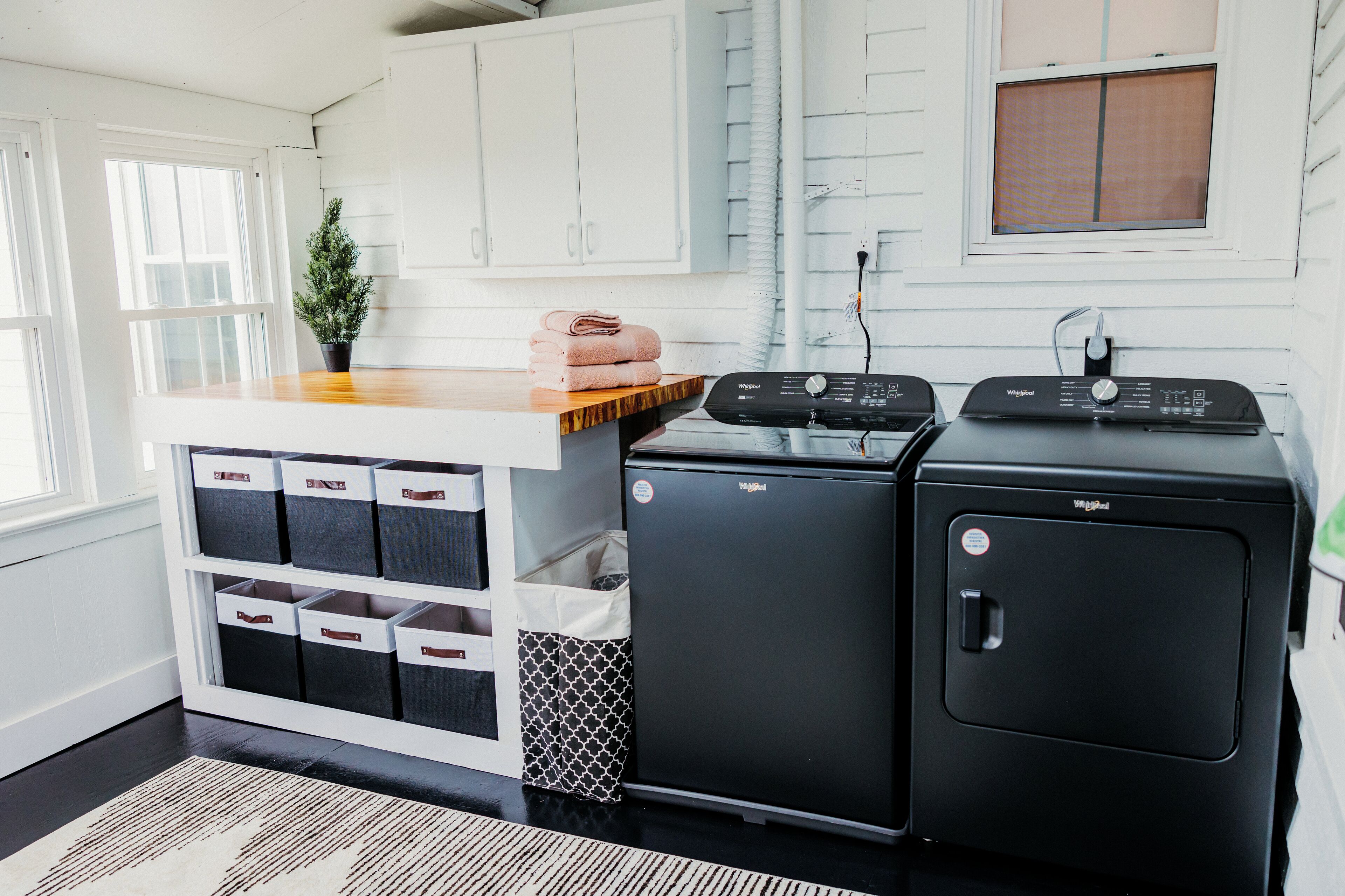 Una cocina compacta con armarios blancos, una encimera de madera, un refrigerador pequeño y una lavadora.