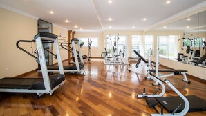 Ein geräumiger Fitnessraum mit unterschiedlichen Trainingsgeräten, großen Fenstern und einem geschliffenen Holzboden.