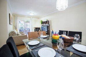 A dining area with a glass table set for four, a sofa, and a kitchen in the background.