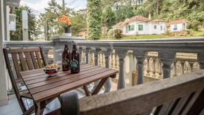 Ein Holztisch mit zwei Bierflaschen und einer Schüssel Snacks auf einem Balkon mit Blick auf ein Wohngebiet mit Häusern und Bäumen.