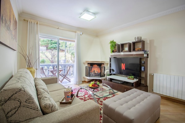 A living room with a sofa, ottoman, glass coffee table, fireplace, TV, and a dining area with chairs and a table.