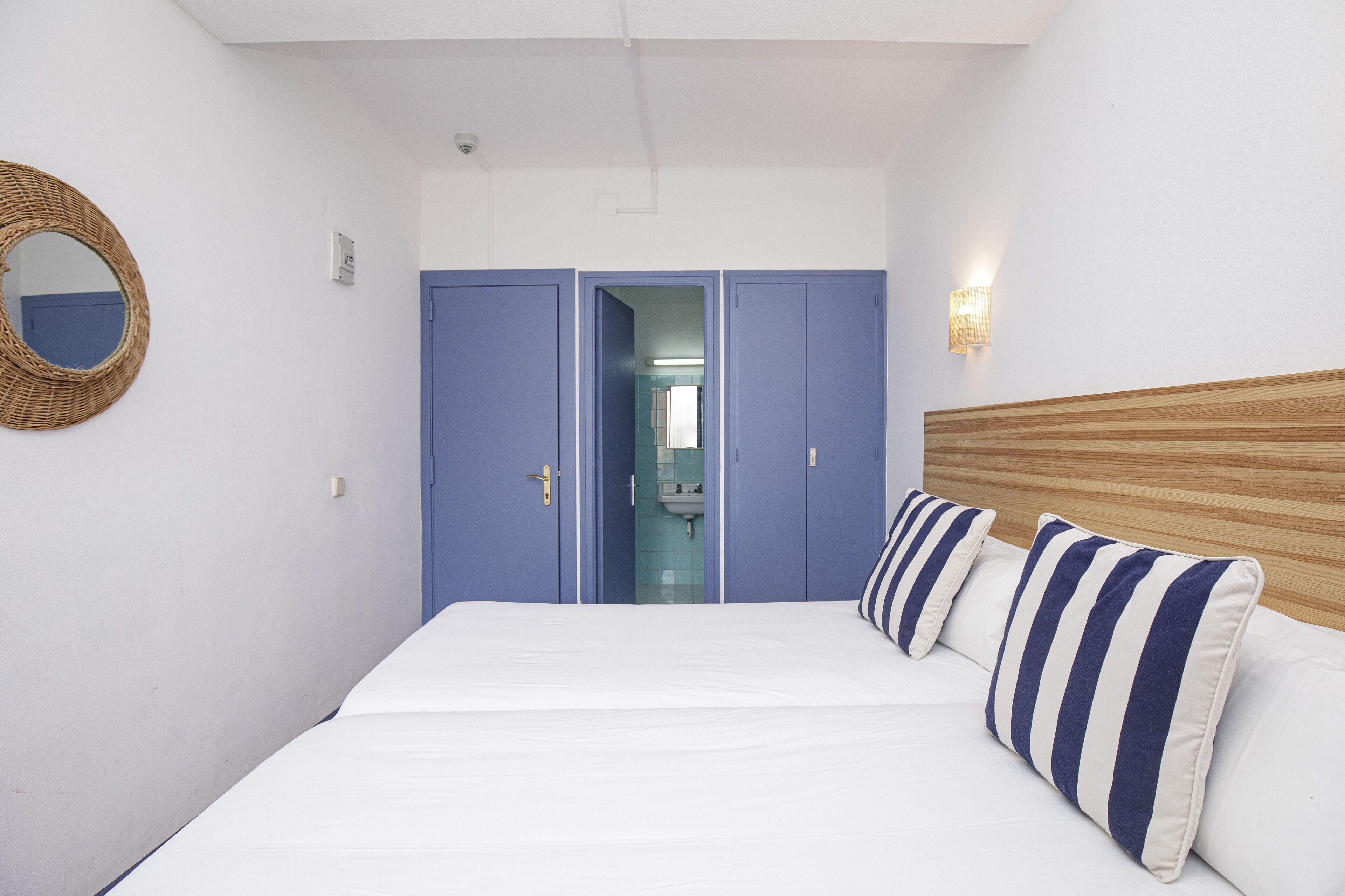 A bedroom with a bed, a wooden headboard, a blue wardrobe, a mirror, and a wall-mounted light fixture.