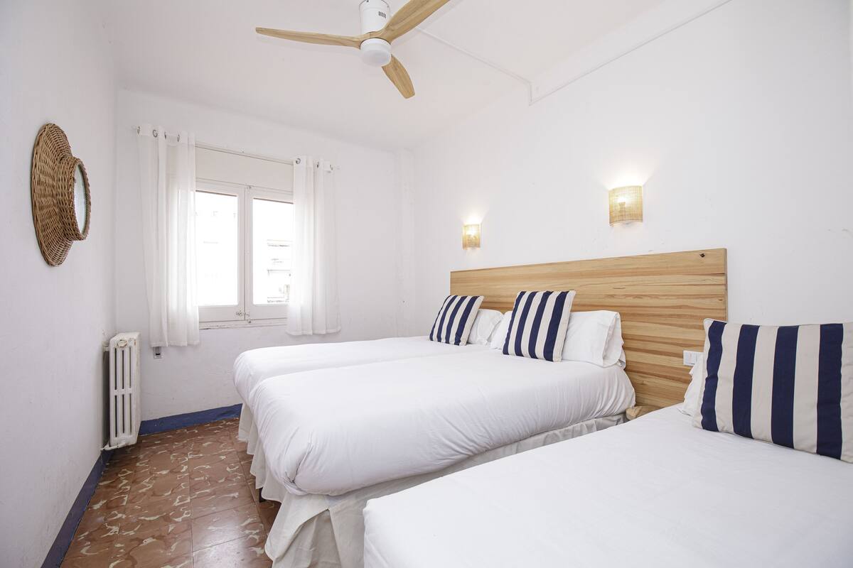 Ein Hotelzimmer mit zwei Betten, einem Deckenventilator, einem Fenster mit Vorhängen und einer Wandleuchte.