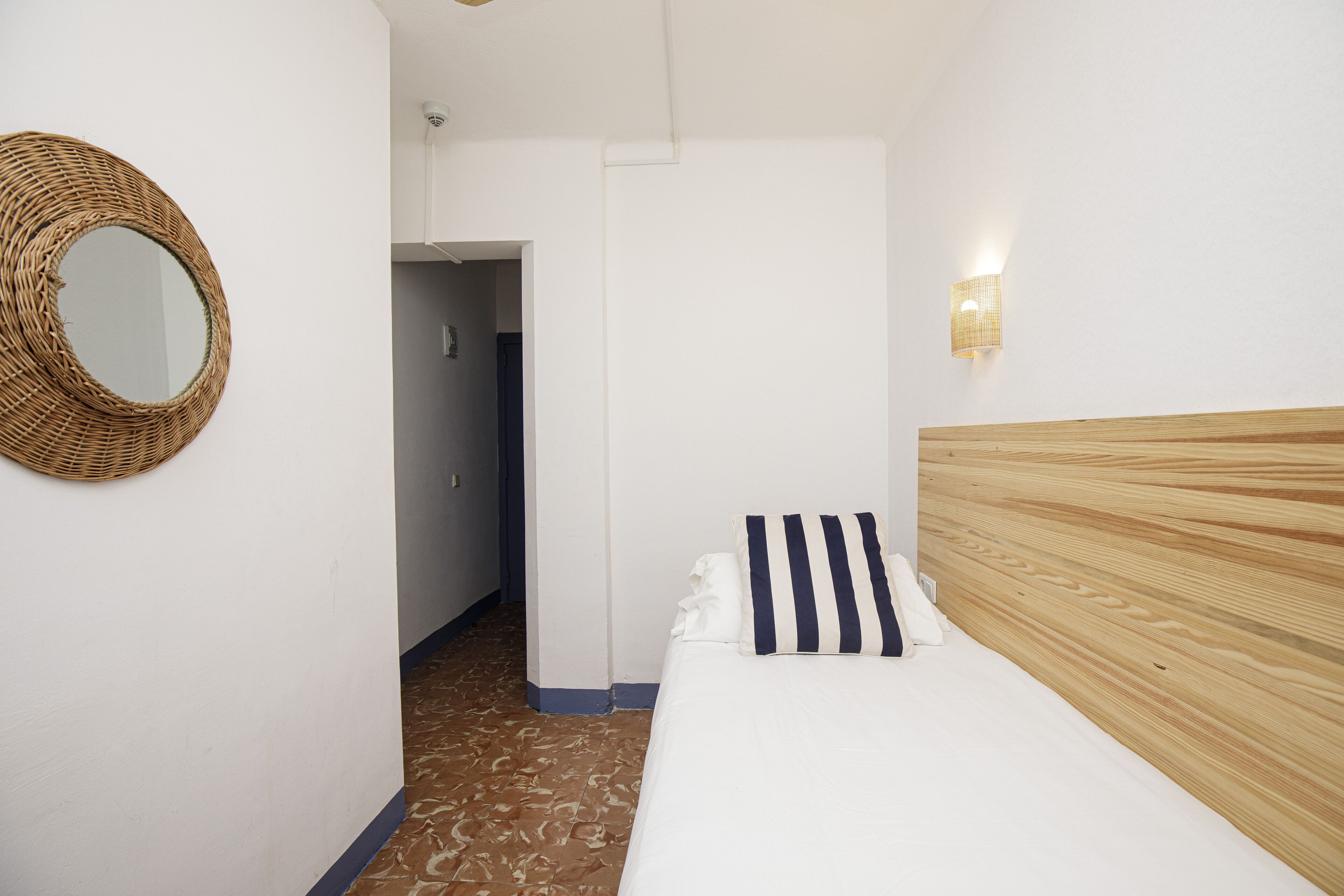 A bedroom with a wooden headboard, a striped pillow, a woven wall hanging, and a light fixture on the wall.