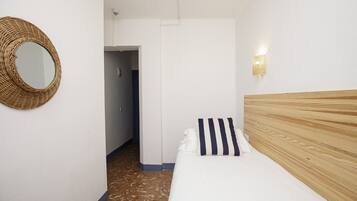 Un dormitorio con cabecera de madera, almohada a rayas, tapiz de pared tejido y una lámpara en la pared.