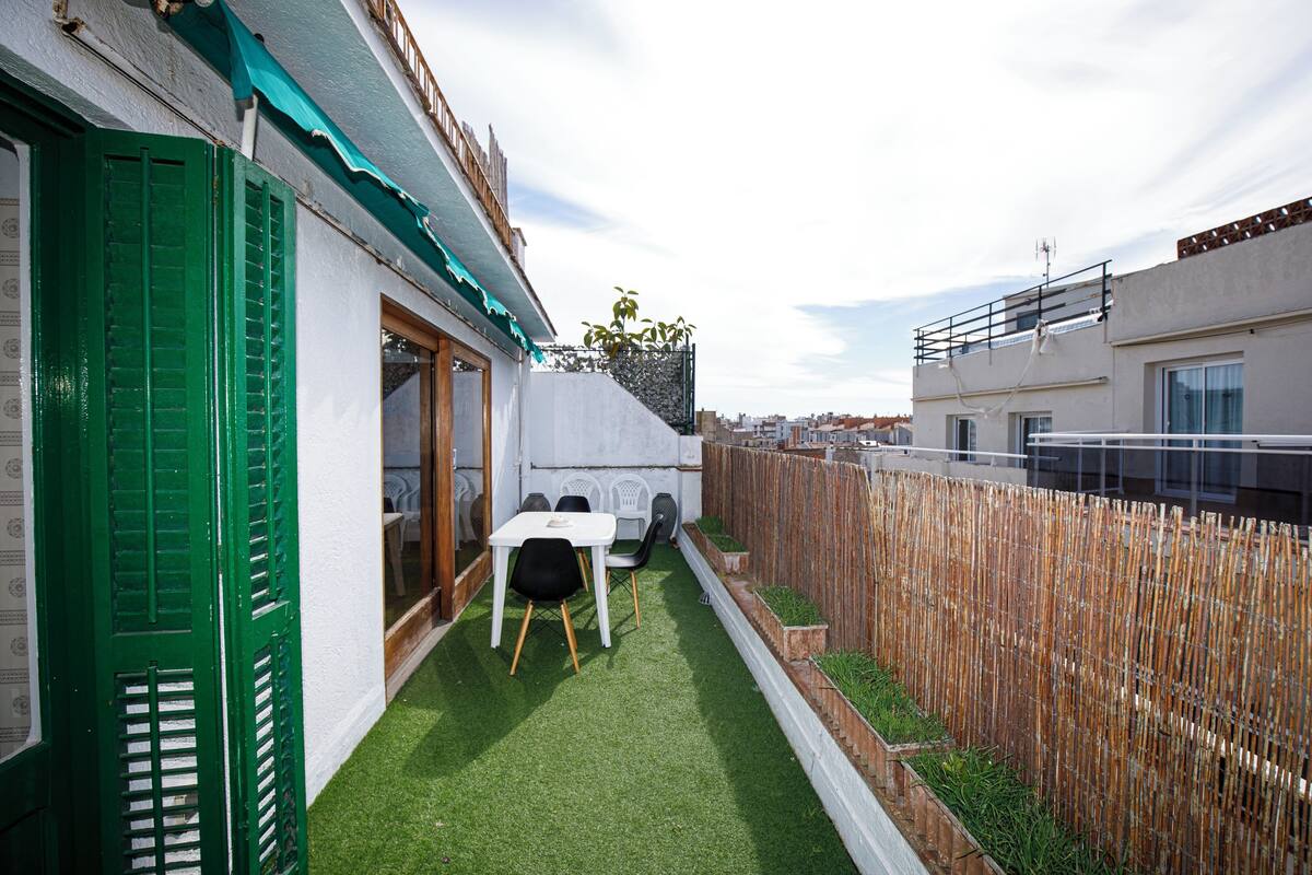 Eine schmale Außenpatio mit künstlichem Gras, einem Holzzaun und einem weißen Tisch mit Stühlen.