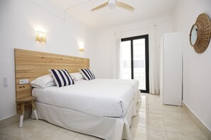 A bedroom with a wooden headboard, a bed with white bedding, a small wooden stool, a white wardrobe, and a ceiling fan. - Hotel Casa Mas (Lloret de Mar)