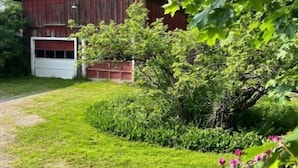A red barn with a white garage door, surrounded by lush green grass and trees. - 1878 Victorian Charmer (Endicott)