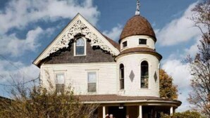 A large, white house with a distinctive tower and a wrap-around porch. - 1878 Victorian Charmer (Endicott)