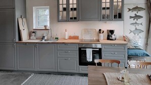 A kitchen with grey cabinets, a wooden countertop, a sink, a coffee maker, and a fish wall art. - Small house in cozy village near the sea (Ystad)