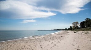 A wide sandy beach with gentle waves, a clear sky, and a distant tree line. - Small house in cozy village near the sea (Ystad)