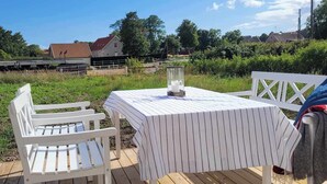 An outdoor patio with a table and chairs, a view of a house, and a fenced area. - Small house in cozy village near the sea (Ystad)