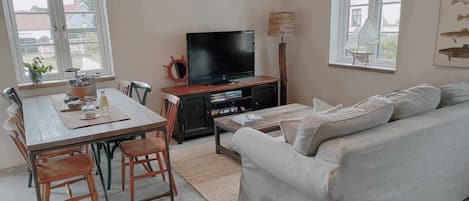 A cozy living room with a dining area, a flat-screen TV, a sofa, and a lamp.