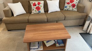 A living room with a brown sofa, white and red floral pillows, a wooden coffee table, and a bookshelf with books. - Poppy, dog-friendly caravan with panoramic sea views on Rockley Park Poole wi-fi (Poole)