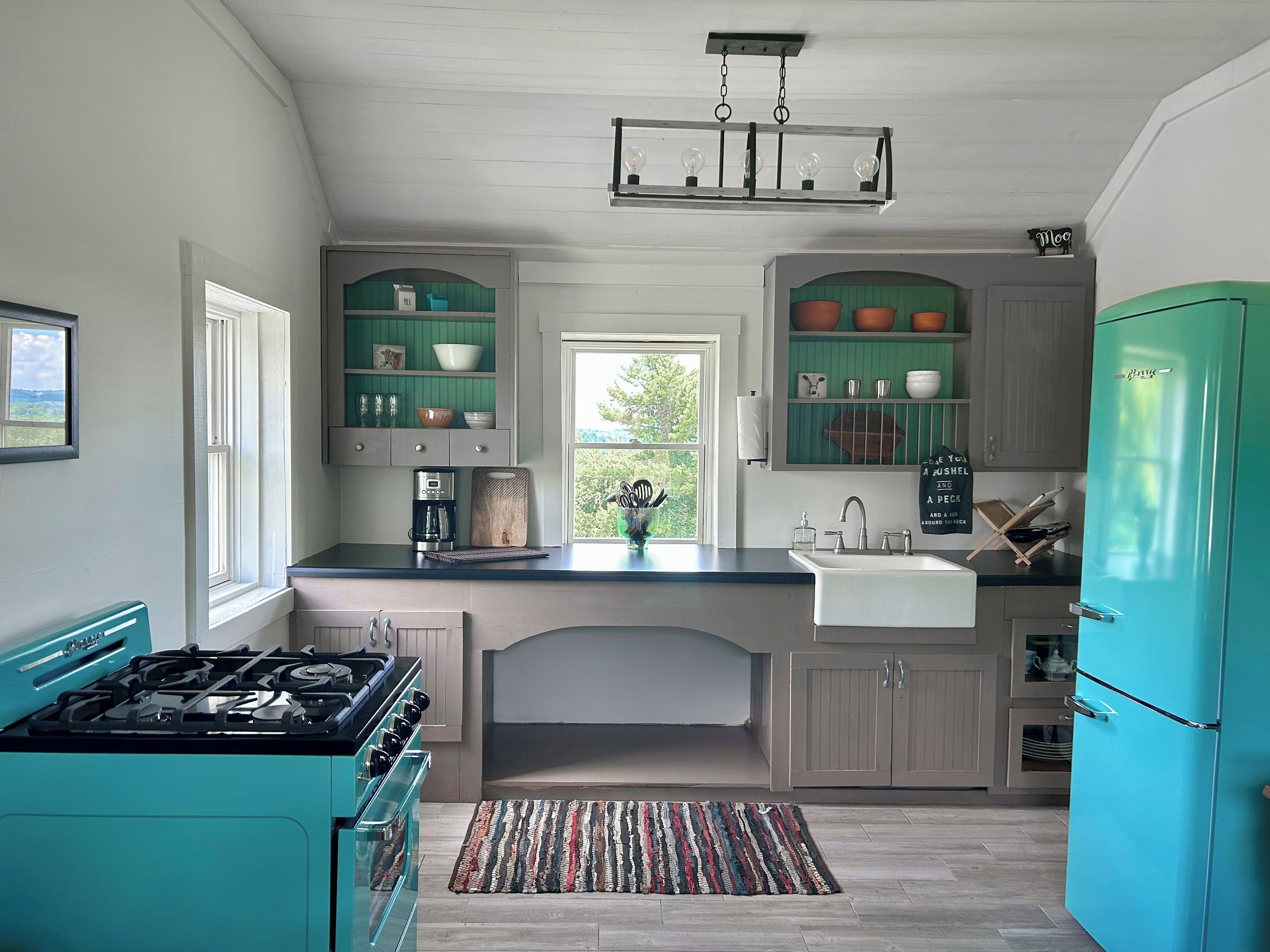A kitchen with teal appliances, a gas stove, a sink, and a window with a view of greenery.