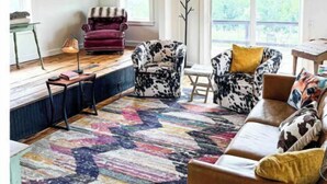 Un salón amplio con techo alto, un ventanal grande y un tapete colorido.