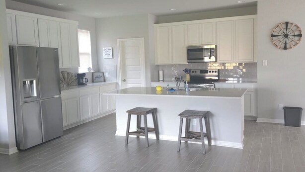 A modern kitchen with white cabinets, stainless steel appliances, and a central island with stools. - Country Cozy! Well stocked, immaculate home. Great short or extended stays!   
 (Jarrell)