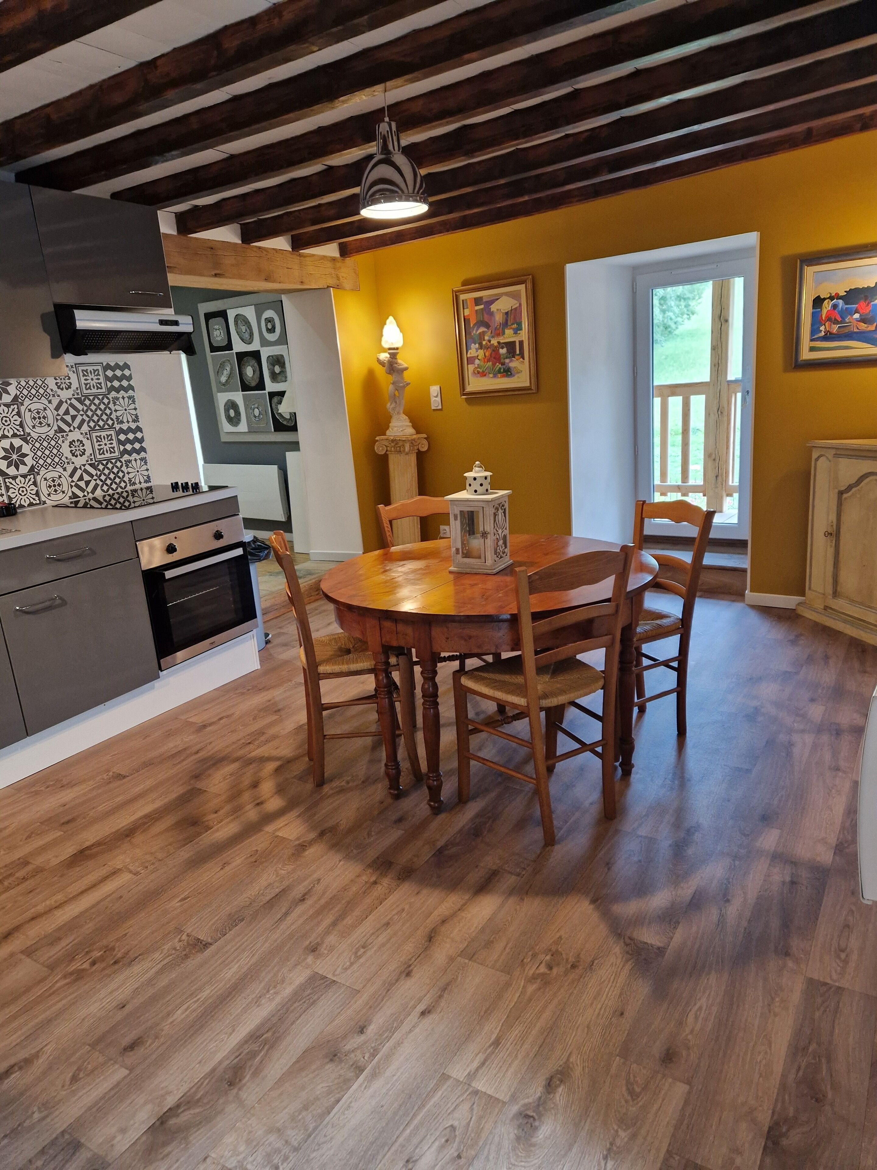 Un comedor con mesa y sillas de madera, una araña y una cocina con estufa y alacenas.