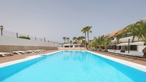 Ein Swimmingpool mit Liegestühlen, Palmen und einem Gebäude mit weißer Fassade.