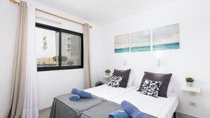 Ein Schlafzimmer mit zwei Betten, einem Fenster mit Vorhängen, Meerblick und einer Wand mit drei Bildern.