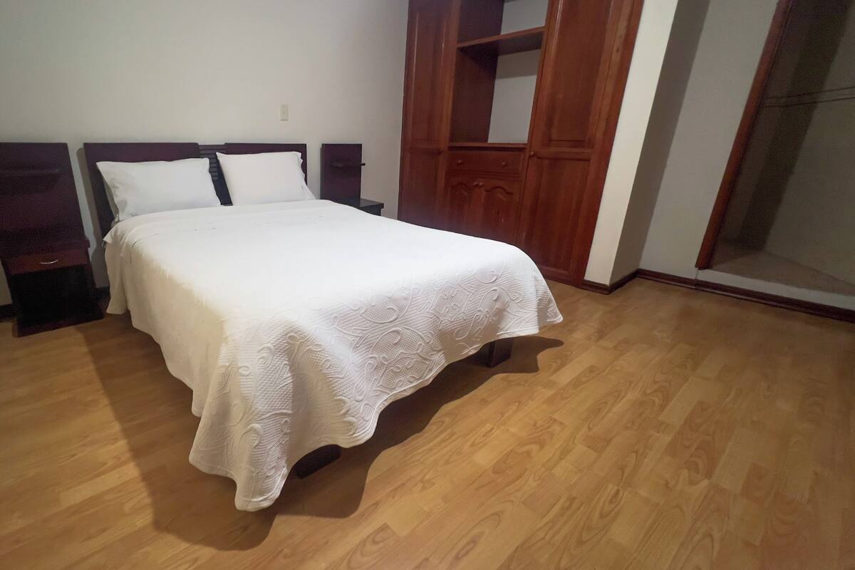 A bedroom with a wooden bed, white bedding, and a wooden floor.