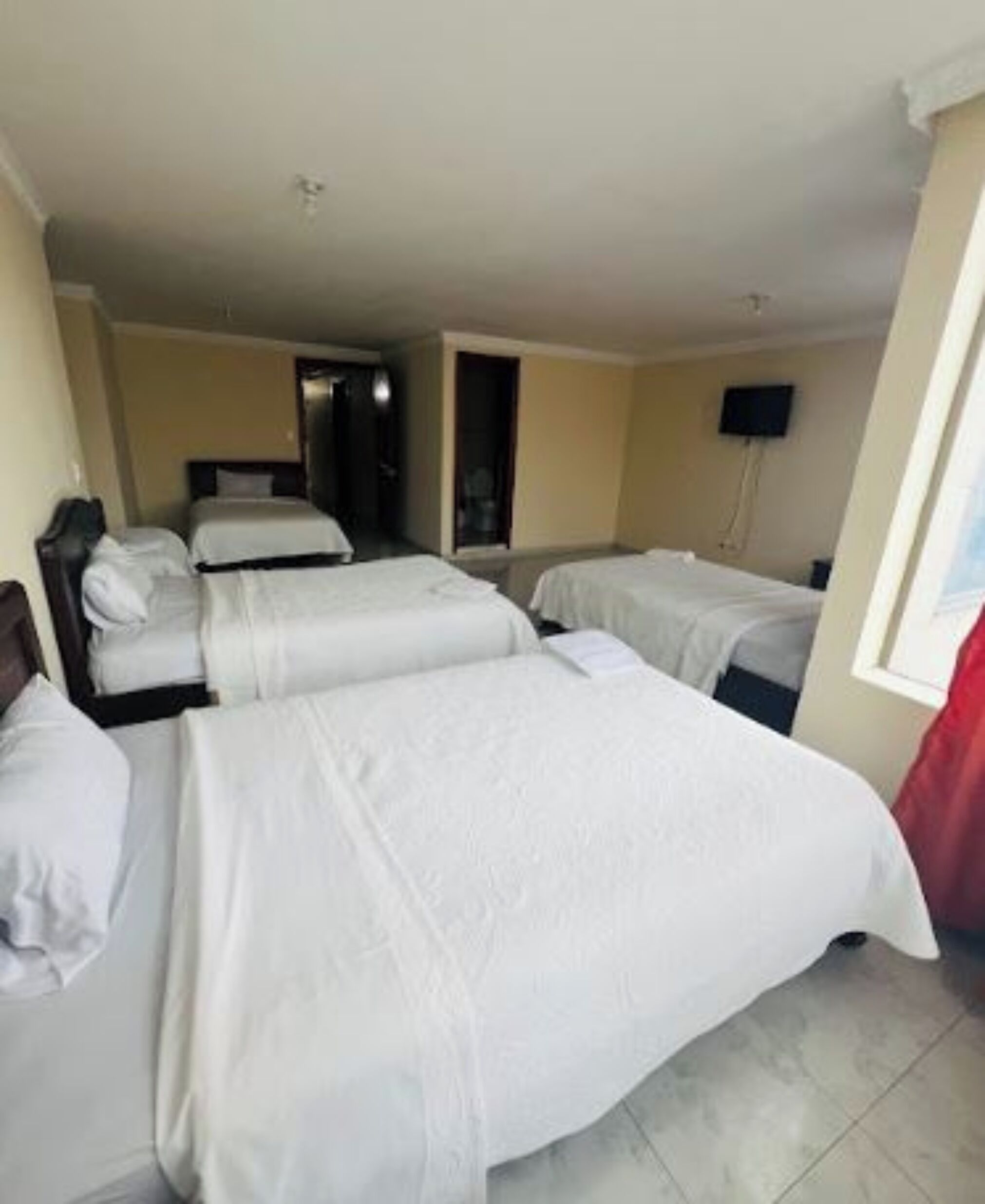 A hotel room with two single beds, a television on the wall, and a door leading to another room.