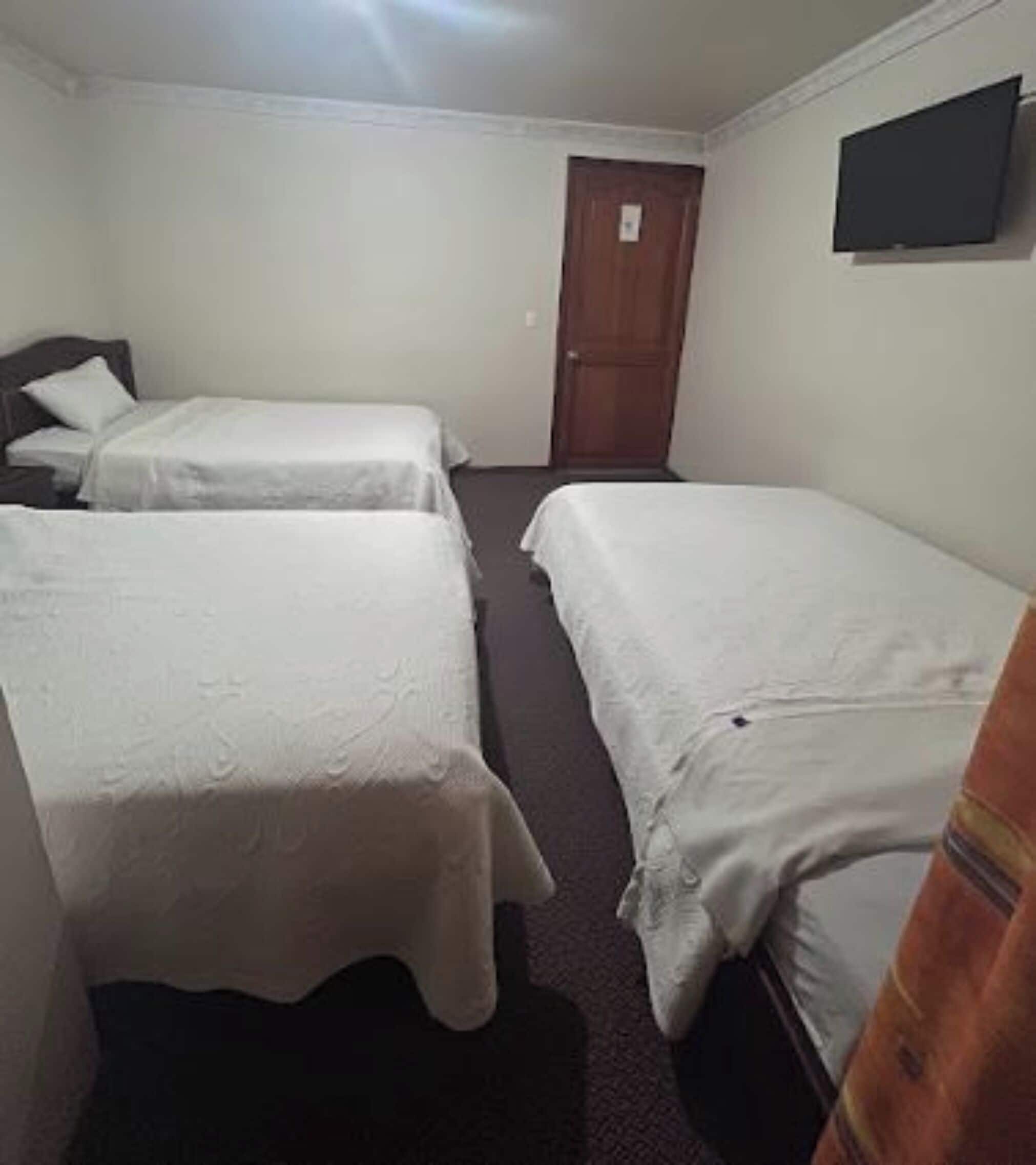 A room with two single beds, a wooden door, and a flat-screen TV mounted on the wall.