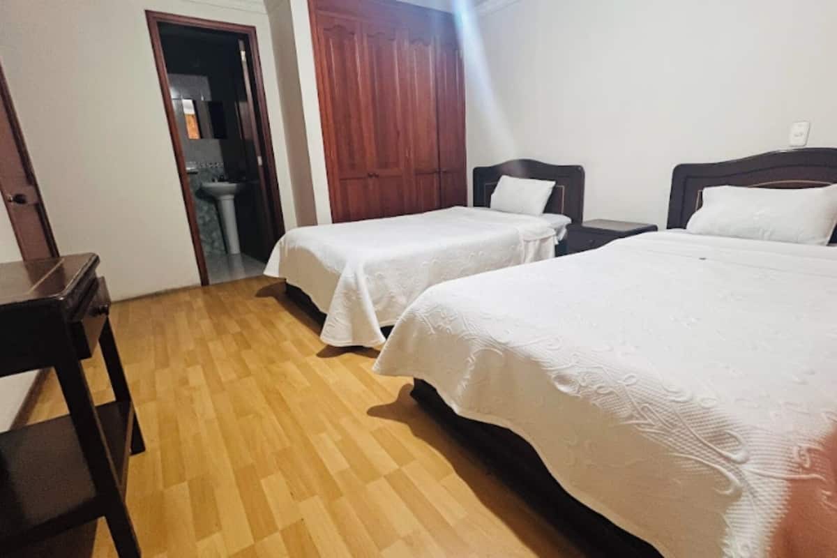A room with two single beds, a wooden floor, a desk, and a wardrobe.
