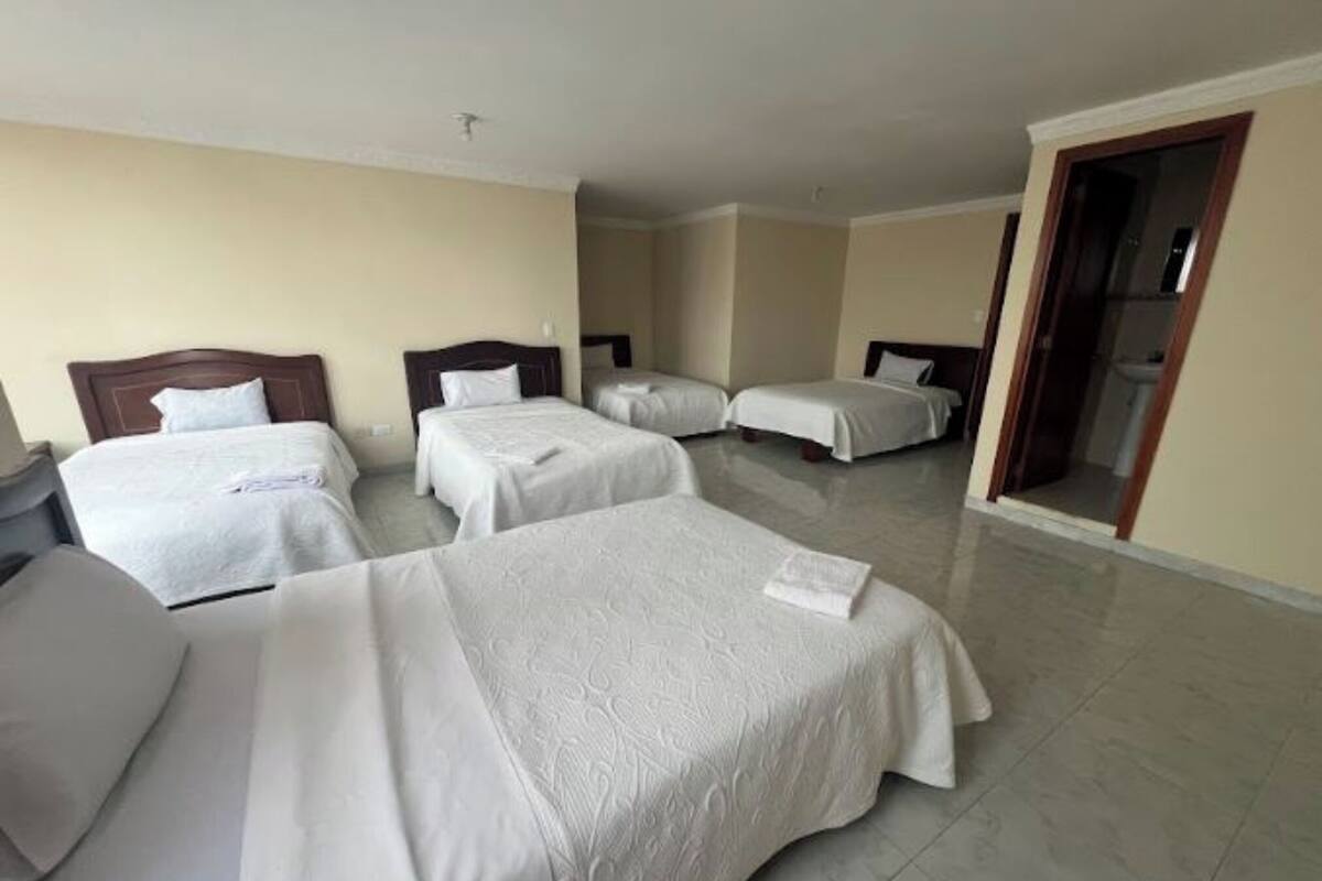 A hotel room with four single beds, a wooden headboard, and a bathroom visible through an open door.
