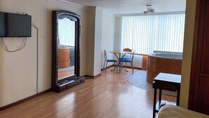 Et hotelværelse med et stort spejl, et fjernsyn ophængt på væggen, et lille bord med to stole og et badekar.