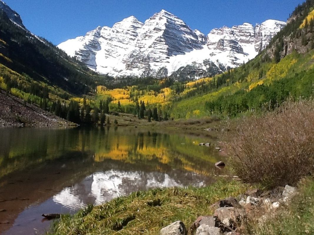 Un lac de montagne aux eaux miroitantes, entouré de collines boisées et de sommets enneigés.