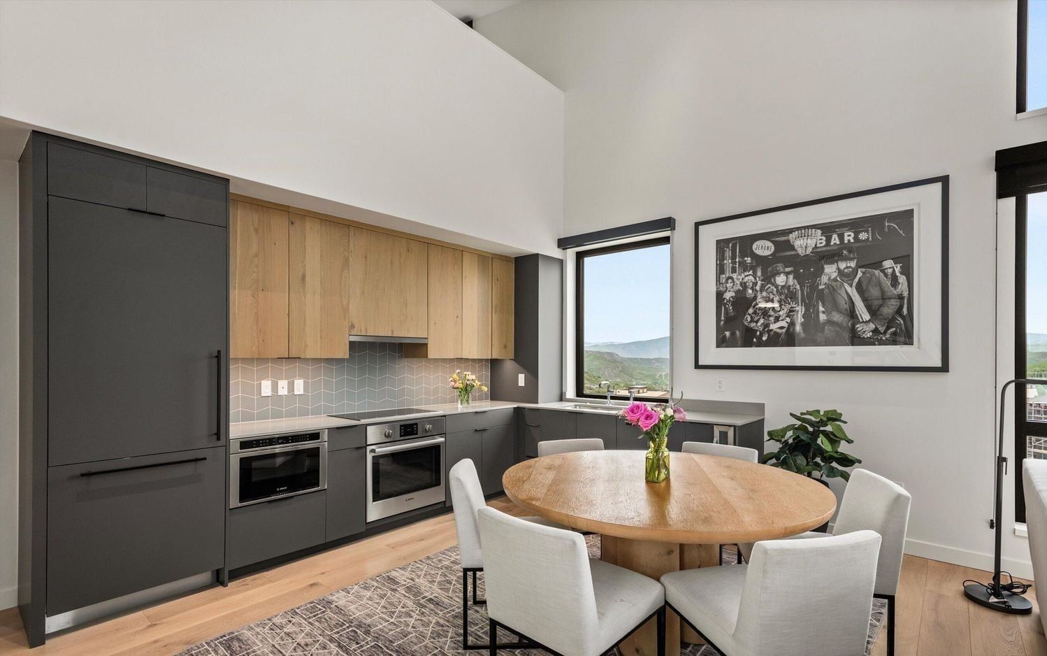 Una cocina moderna con armarios oscuros, encimera de madera y comedor con mesa y sillas redondas.