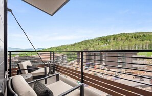 A balcony with a view of a construction site and a forested hill.