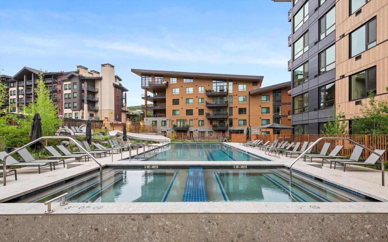 Une piscine avec des chaises longues et, en arrière-plan, un ensemble de bâtiments modernes.