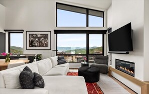 A modern living room with a large sofa, a flat-screen TV, and a fireplace. - Charlie Rentz: Penthouse Ski-In/Out, Sleeps 10, Pool + Waterslide, Snowmass Base Village (Snowmass Village)
