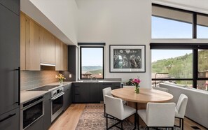 A modern kitchen with a dining area, large windows, and a view of the outdoors.