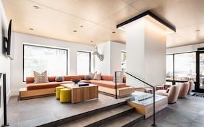 A modern living room with a sofa, ottoman, coffee table, and a glass display unit. - Charlie Rentz: Penthouse Ski-In/Out, Sleeps 10, Pool + Waterslide, Snowmass Base Village (Snowmass Village)