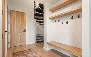 A hallway with a wooden door, a staircase, and a pegboard wall with hooks.