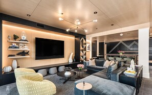 A modern living room with a large flat-screen TV, comfortable seating, and a decorative wall with a geometric light pattern. - Charlie Rentz: Penthouse Ski-In/Out, Sleeps 10, Pool + Waterslide, Snowmass Base Village (Snowmass Village)