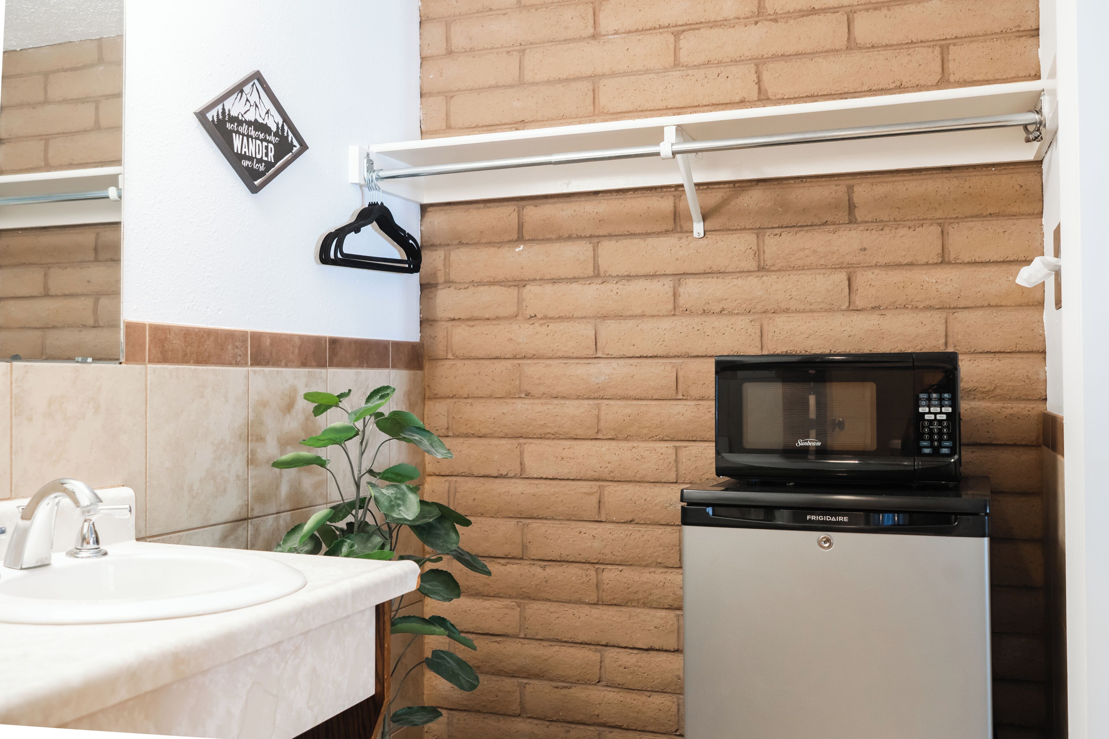 Une salle de bain équipée d’un lavabo, d’un miroir, d’un porte-serviettes, d’une plante, d’un four à micro-ondes et d’un petit réfrigérateur.