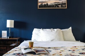 A hotel room with a bed, a nightstand, a lamp, a framed picture on the wall, and a book on the bed.
