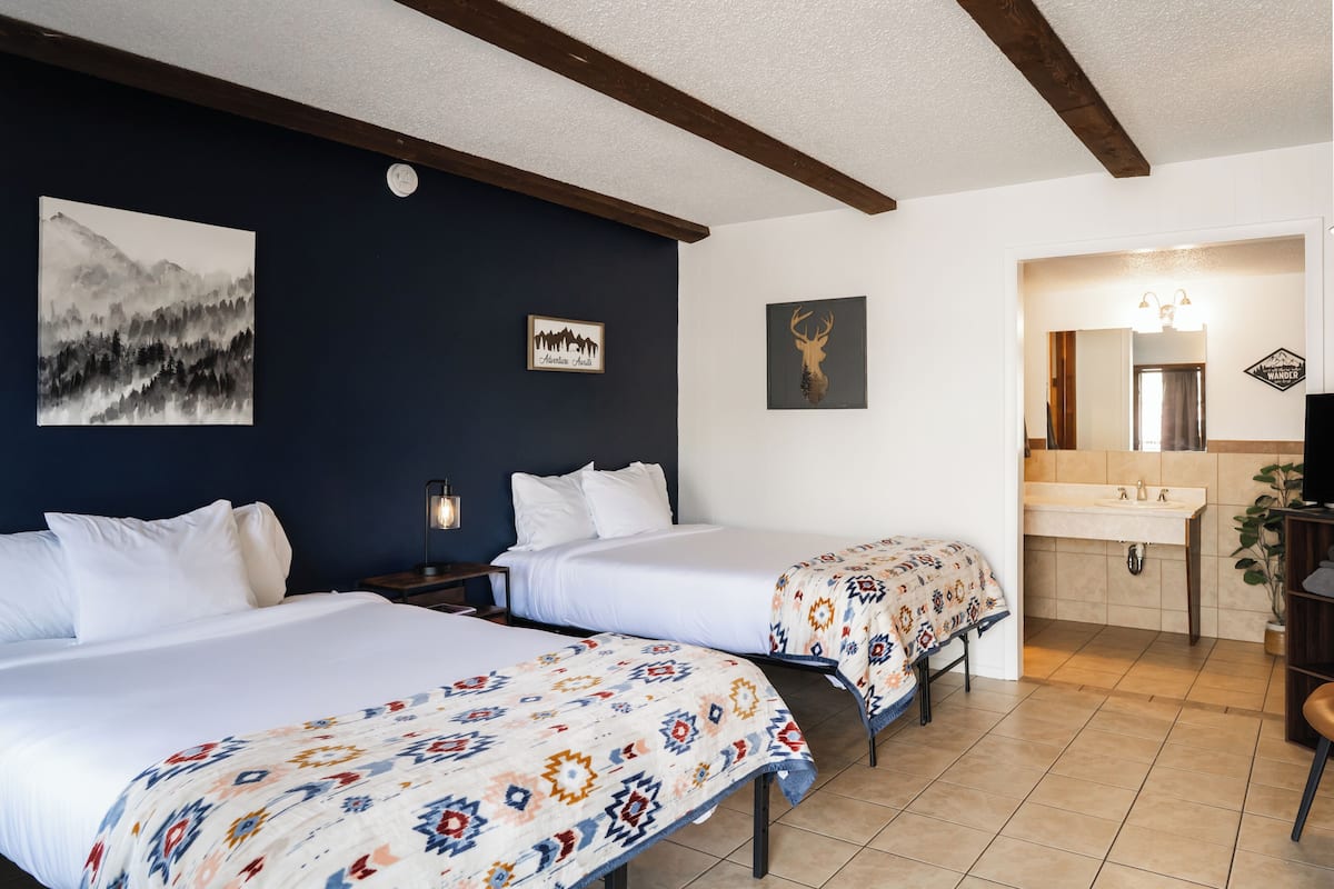 A hotel room with two beds, a large painting, a framed picture, a mirror, and a bathroom with a sink.