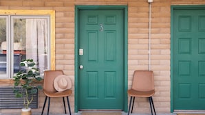 A green door with the number 3, two brown chairs, and a potted plant.
