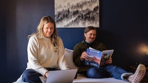 Two people sitting on a bed with a laptop and a book.