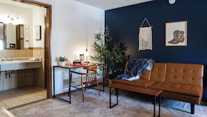 A room with a sofa, a dining table, chairs, a potted plant, a wall-mounted plant, and a framed picture.
