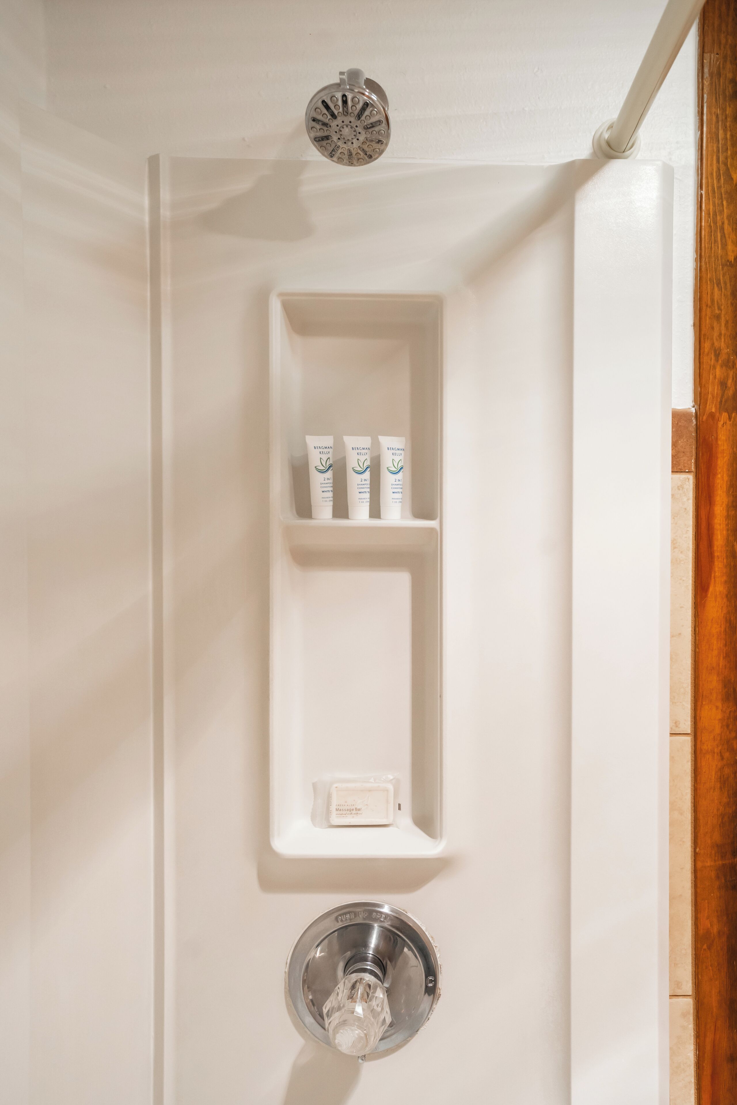 A bathroom with a white vanity, a showerhead, and a shelf with toiletries.