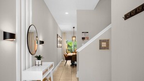 A hallway with a white console table, a mirror, a potted plant, a dining area with a table and chairs, and a staircase. - 4 BD/ 3 BA/ Paradise Palms (2955 BP) (Kissimmee)