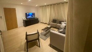 Una sala de estar moderna con un televisor de pantalla plana, un sofá, un sillón y una mesa de centro.
