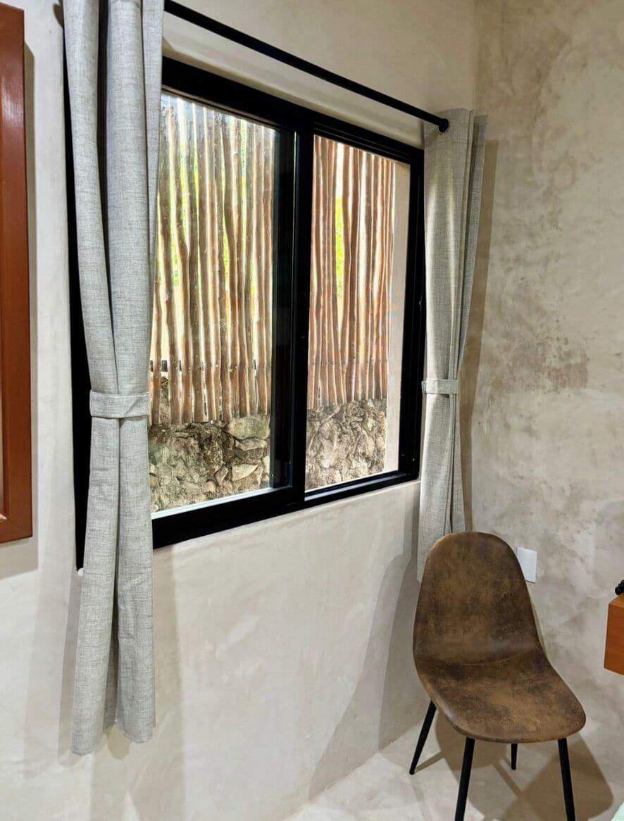 Una habitación con ventana, cortinas, una silla y una pared con textura.